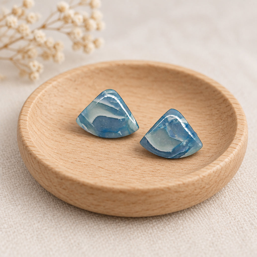A pair of small triangular stud earrings made from light blue marbled resin, displayed on a plain white surface.
